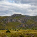 A scenic view of a rocky mountain range with lush greenery under a cloudy sky.